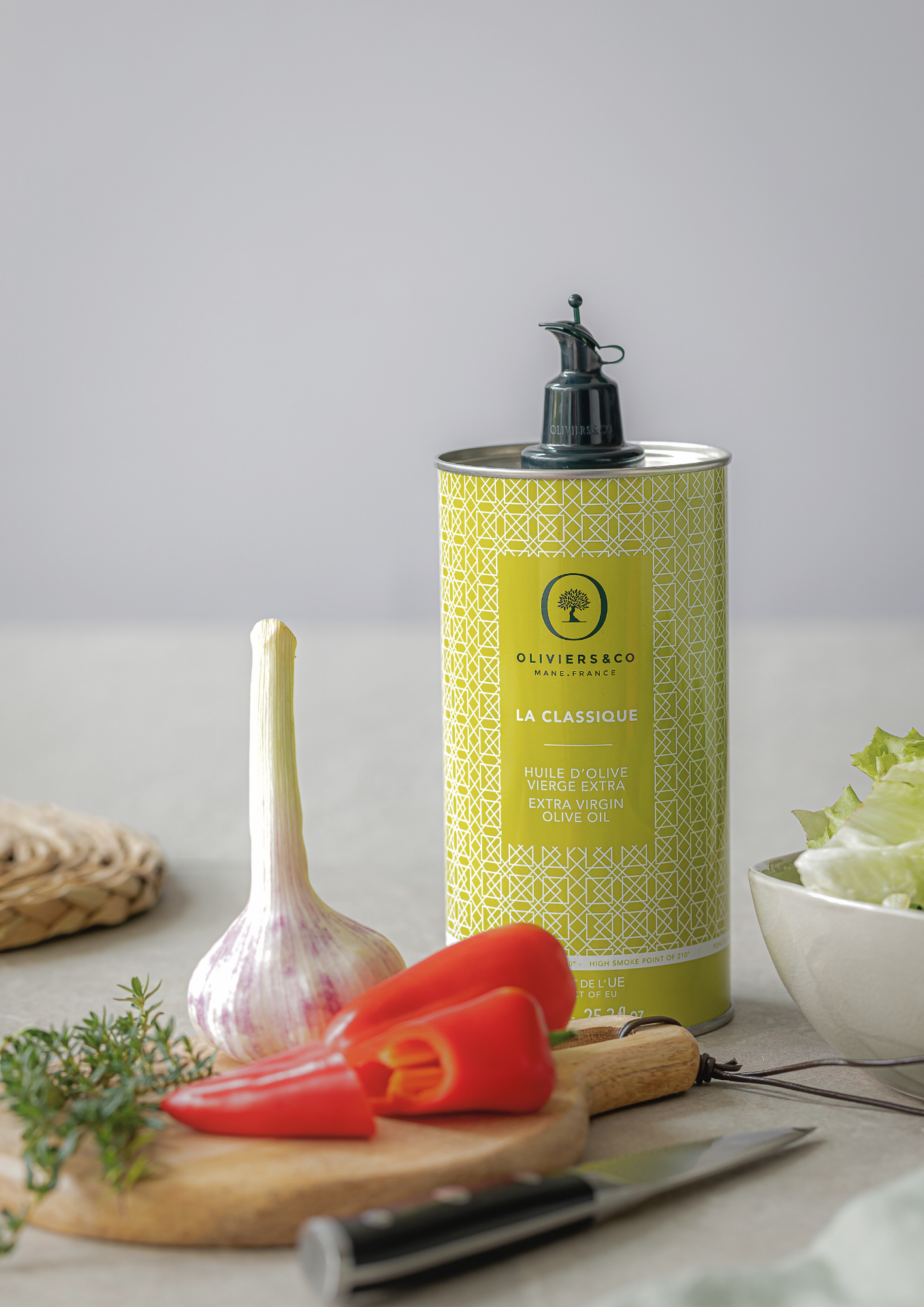 Bouteille d’huile d’olive extra vierge Oliviers & Co posée près d’une planche et d’un couteau de cuisine, utilisés pour préparer des légumes.