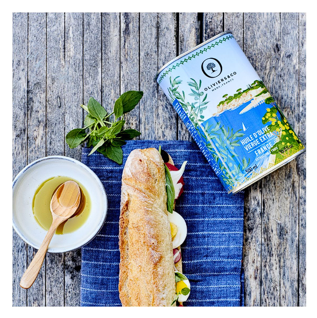 extra panenský olivový olej Francie 500 ml plechovka extra panenského oleje 500 ml původem z Francie položená na utěrce s sendvičem a miskou na olej